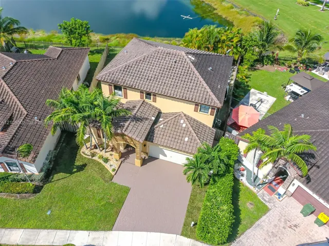Two-story residence featuring a tile roof, paved driveway, arched entryway, and landscaped yard backing to a water feature