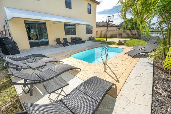 Backyard featuring a concrete pool with a metal handrail, a stamped concrete patio, a retractable awning, and a built-in basketball hoop