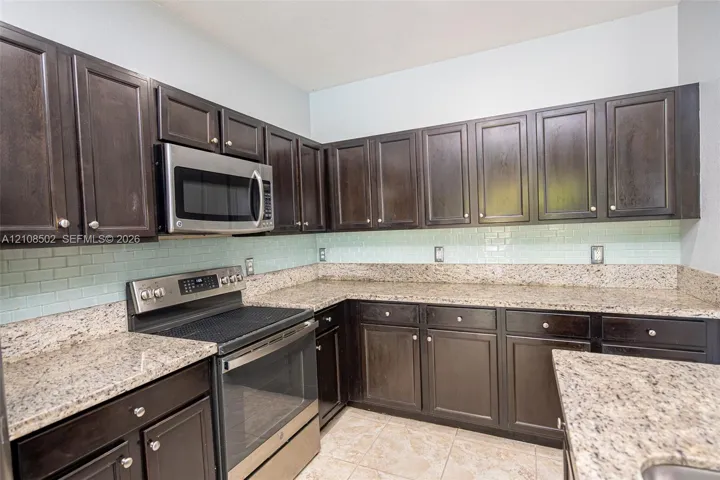Kitchen featuring dark wood cabinetry, stone-surface countertops, subway-style tile backsplash, and stainless steel appliances