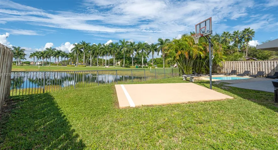 Backyard featuring a paved basketball court, swimming pool, fenced perimeter, and waterfront scenery