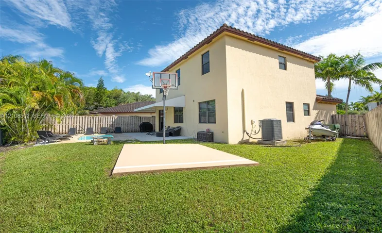 Backyard featuring a stucco-exterior residence, a concrete patio, an in-ground swimming pool, a dedicated basketball court, and perimeter wood fencing