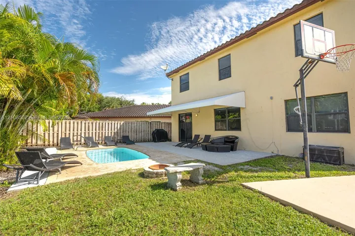 Exterior space featuring a concrete patio, in-ground swimming pool, stone fire pit, and a concrete sports pad