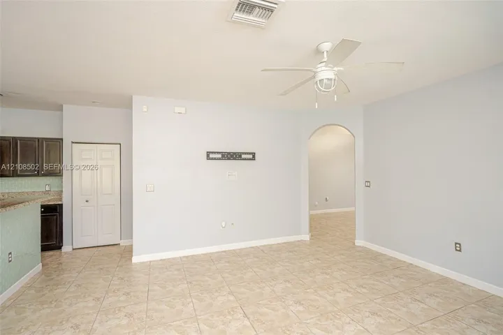 Open interior area featuring tile flooring, a white ceiling fan with integrated lighting, and an arched doorway