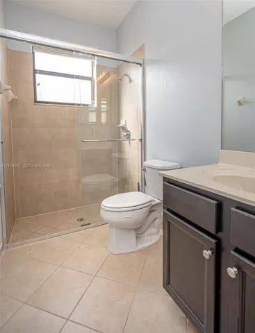 Bathroom featuring a glass-enclosed walk-in shower with tile surround, dark wood-finish cabinetry, and a solid-surface vanity countertop