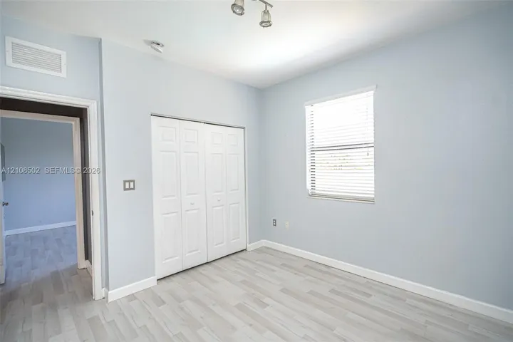 Room featuring wood-finish flooring, a double-panel closet with white doors, a single window with horizontal blinds, and a multi-bulb ceiling-mounted light fixture