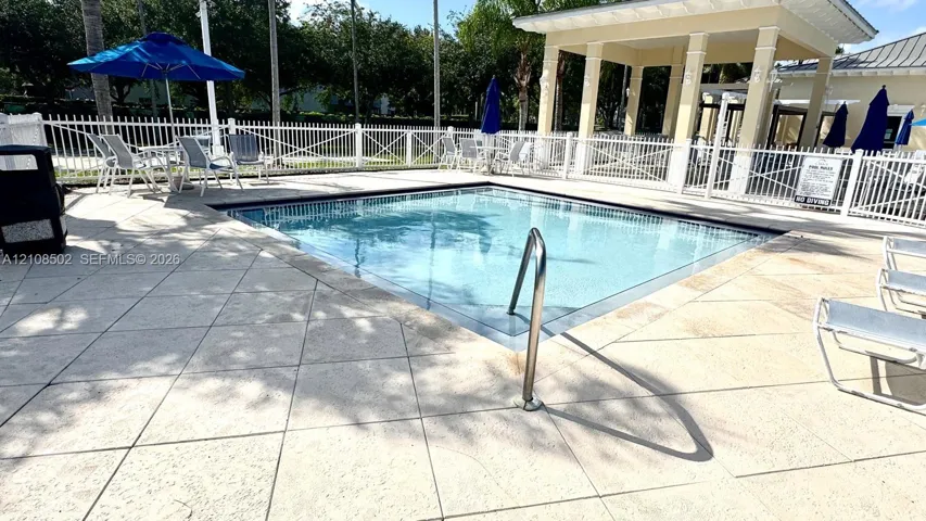 Swimming pool with tile deck surround, metal handrail, and covered pavilion structure enclosed by perimeter fencing