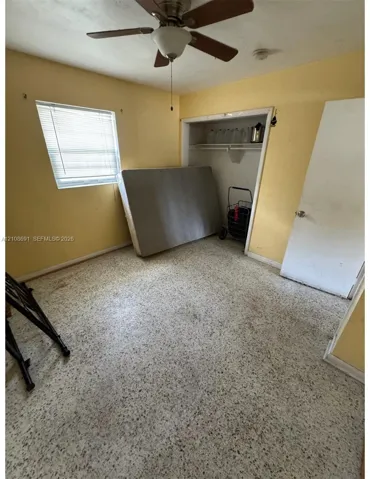 Interior space featuring terrazzo flooring, a ceiling fan with light fixture, a single-hung window with blinds, and a built-in closet with shelving