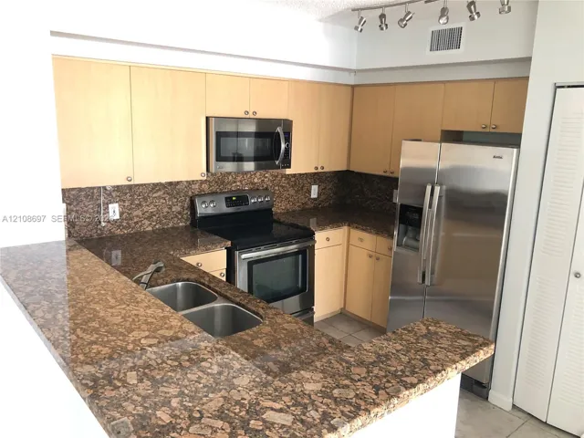 Kitchen featuring light-finish cabinetry, natural stone countertops, stainless steel appliances, and a double-basin under-mount sink with track lighting