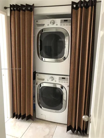 Stacked white front-load washer and dryer with chrome-finished doors, set within a recessed alcove featuring tile flooring