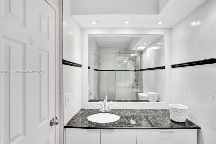 Bathroom featuring a stone-surface vanity with an integrated basin, high-gloss white cabinetry, large-format wall tiling with a dark decorative accent border, and a glass-enclosed shower stall with sliding hardware