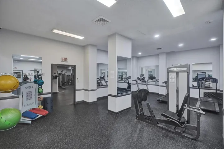 Fitness room featuring rubberized flooring, recessed ceiling lighting, wall-to-wall mirrors, and structural columns