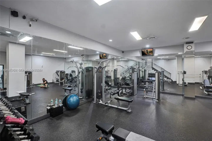 Fitness center featuring rubber flooring, floor-to-ceiling wall mirrors, recessed lighting, and a staircase