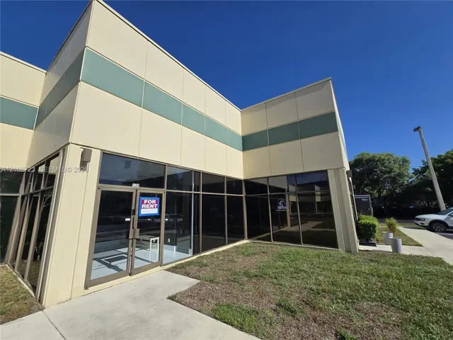 Commercial exterior featuring metal panel facade, extensive floor-to-ceiling glass windows, and concrete walkway