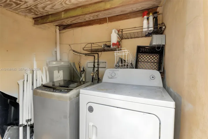 Laundry area featuring concrete block walls, exposed wood ceiling joists, and integrated wall-mounted wire shelving