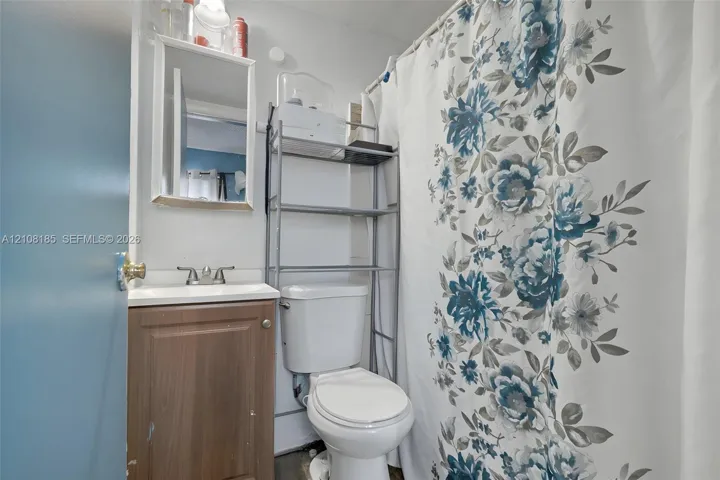 Bathroom featuring a vanity with a white basin, dual-handle faucet, and wall-mounted mirror, alongside a standard toilet and a shower-tub combination