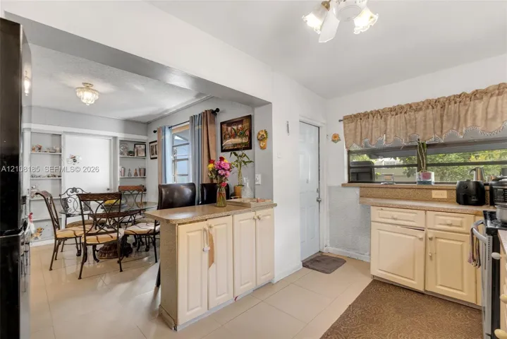 Kitchen featuring light-toned cabinetry, solid surface countertops, built-in shelving, tile flooring, and overhead lighting fixtures