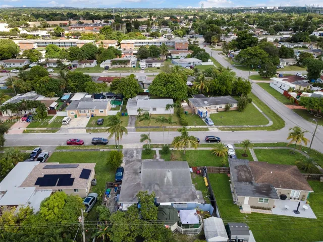 Aerial perspective of a single-story residence featuring a shingle roof, solar panel array, concrete driveway, and fenced perimeter