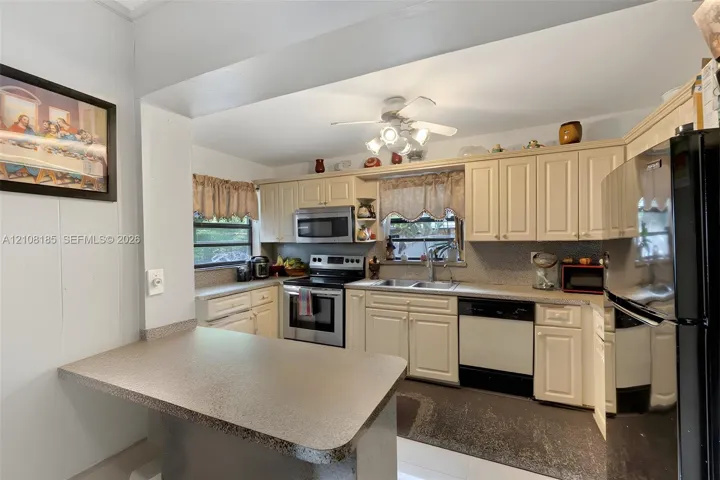 Kitchen featuring shaker-style cabinetry, an integrated breakfast bar, stainless steel appliances, a dual-basin sink, and a ceiling-mounted light fixture