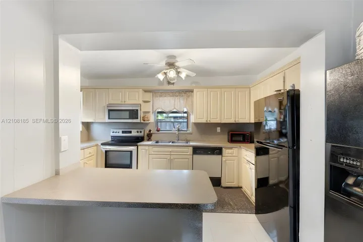Kitchen featuring off-white cabinetry, solid-surface breakfast bar, black full-size refrigerator, integrated microwave, and built-in dishwasher