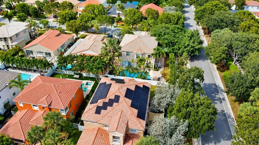 Aerial perspective featuring tile roofing, roof-mounted solar panels, private swimming pools, and mature landscaping