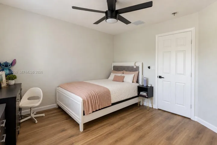 Room featuring wood-finish flooring, a matte black ceiling fan with integrated lighting, and a six-panel door with matte black hardware