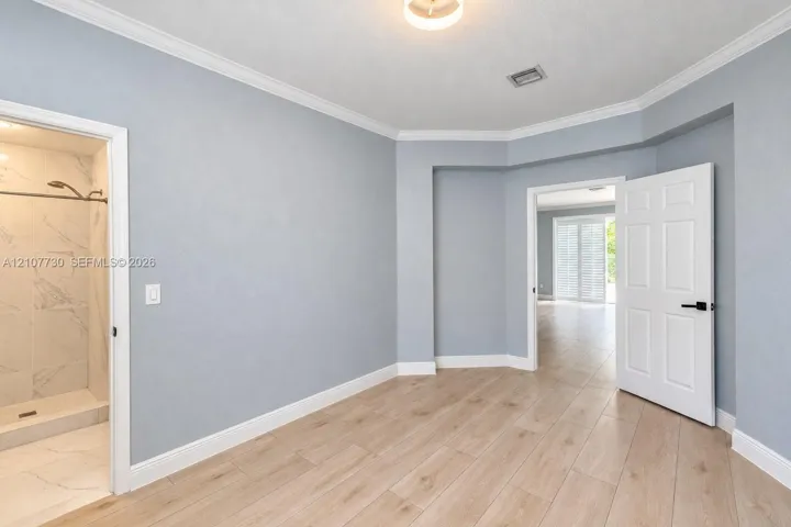 Room featuring wood-finish tile flooring, crown molding, multi-panel doors with matte black hardware, and an en-suite with stone-finish wall tile and a walk-in shower