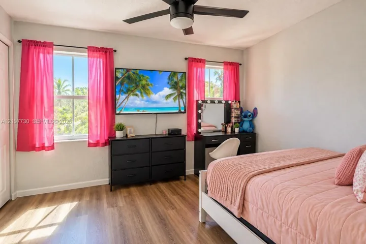 Bedroom interior featuring wood-finish flooring, dual windows with natural light, and a matte black ceiling fan