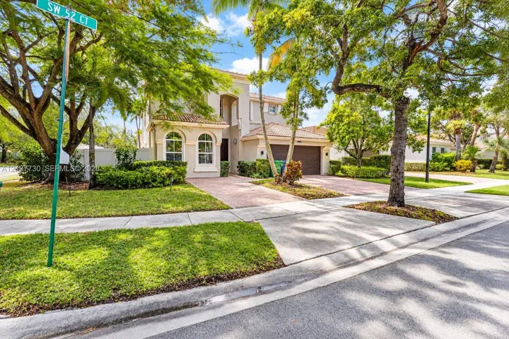 Two-story residence featuring a tile roof, arched windows, concrete paver driveway, and mature landscaping