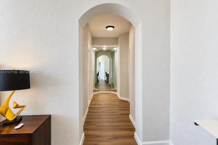Arched doorway featuring wood-finish flooring, neutral wall paint, and mirrored wall panels