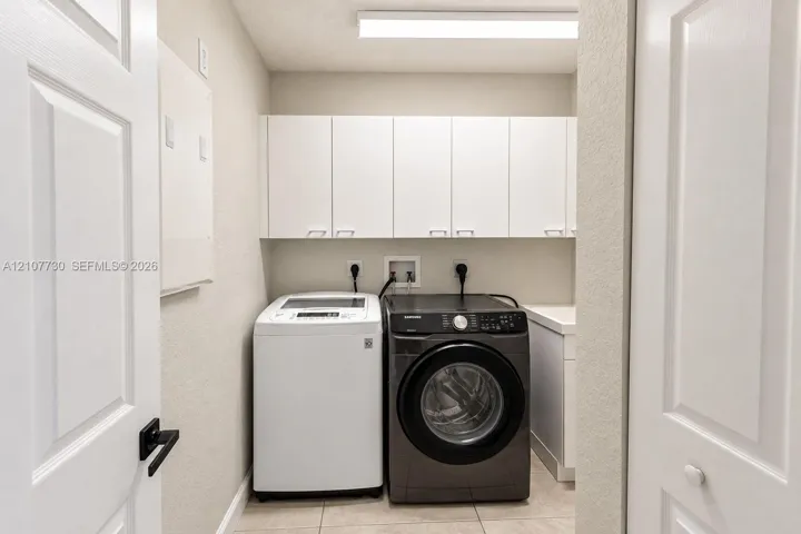 Laundry room featuring white shaker-style wall-mounted cabinetry, tile flooring, and a dedicated utility sink