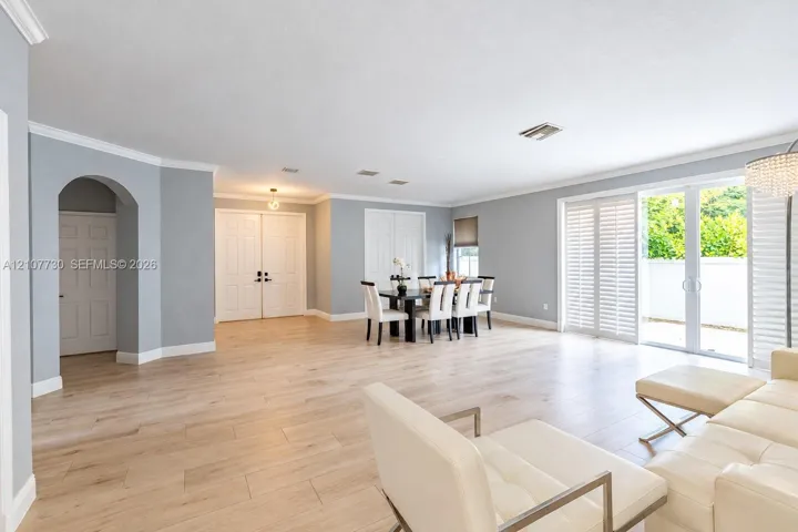 Open-concept living space featuring wood-finish flooring, crown molding, arched entryway, and multi-panel sliding glass doors with plantation shutters