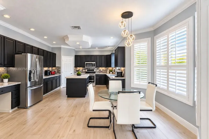 Kitchen featuring dark cabinetry, stone-finish countertops, stainless steel appliances, wood-finish flooring, and crown molding