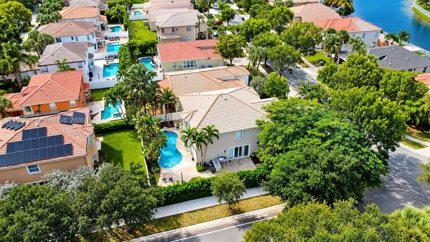 Aerial perspective of a two-story residence featuring a tile roof, an in-ground swimming pool, stone-paver patio, and mature landscaping