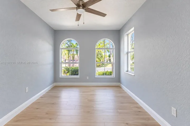 Room featuring wood-finish flooring, two arched windows, a single rectangular window, and a ceiling fan