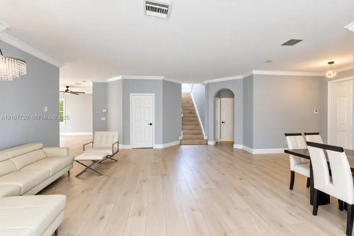 Open-concept interior featuring light wood-finish flooring, crown molding, arched architectural detailing, and a multi-level staircase with carpeted treads