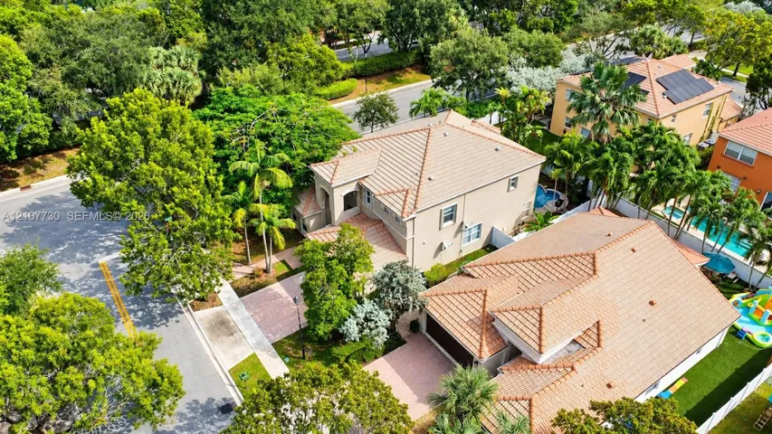Aerial perspective of a multi-story residence featuring a clay tile roof, paved driveway, integrated garage, and mature landscaping