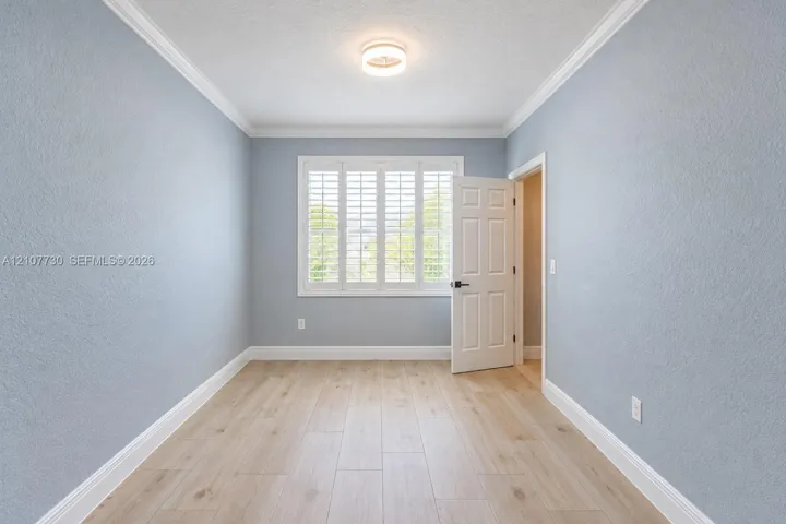 Light-filled interior featuring wood-finish flooring, plantation shutters, crown molding, and a neutral color palette