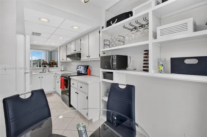 Kitchen featuring white shaker-style cabinetry, solid-surface countertops, tile flooring, recessed lighting, and built-in open display shelving
