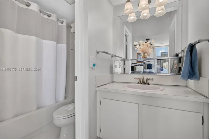 Bathroom featuring a white vanity with integrated sink, metallic widespread faucet, expansive wall-mounted mirror, overhead multi-light fixture, and a combination tub and shower