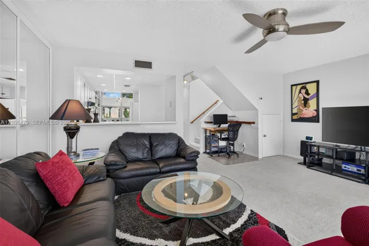Living area featuring mirrored wall closet doors, a brushed-metal ceiling fan with integrated lighting, and an open pass-through window to the kitchen