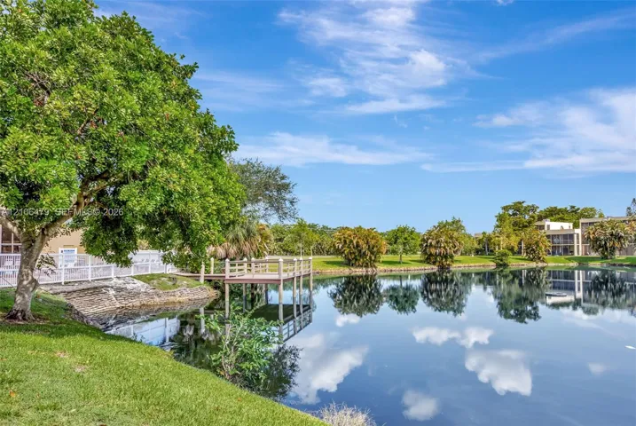 Waterfront grounds featuring a private wooden dock, manicured lawn, mature trees, and stone-reinforced shoreline