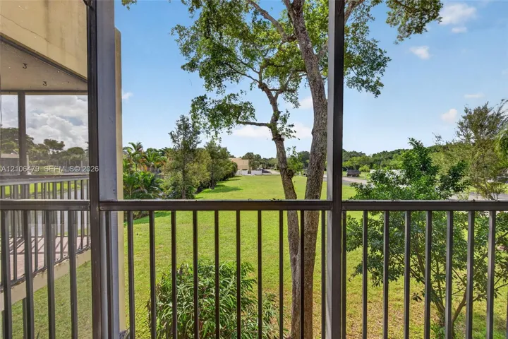 Screened-in balcony featuring metal railings, overlooking an expansive lawn with mature trees