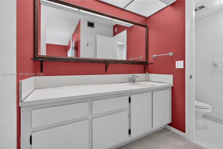 Bathroom featuring a vanity with white cabinetry, a solid surface countertop with an integrated basin, a large wall-mounted mirror with a wood frame, and a separate water closet area