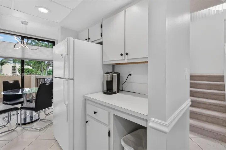 Kitchen area featuring white cabinetry, solid-surface countertops, full-size refrigerator, recessed lighting, and tile flooring