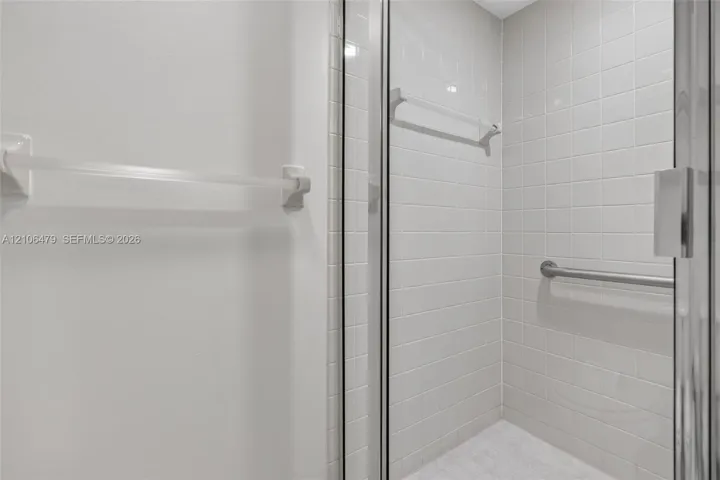 Shower enclosure featuring white wall tiling, a glass door, a wall-mounted metal grab bar, and a horizontal towel rack
