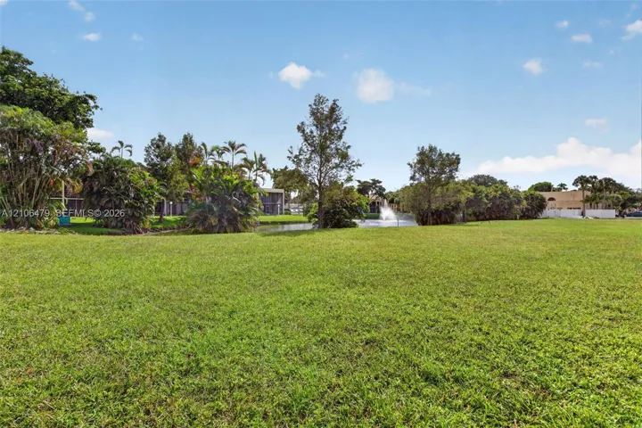 Expansive green space featuring a manicured lawn, pond, water fountain, and mature tropical landscaping