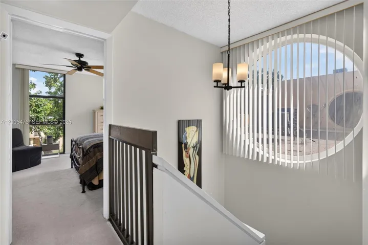 Oval window with vertical blinds, three-light metal chandelier, and decorative wood-finish stair railing