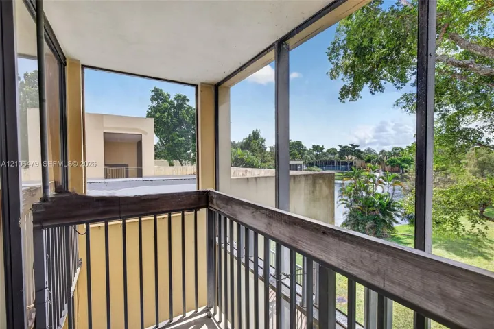 Screened balcony featuring metal railings and wood-finish cap rails overlooking a pond and landscape