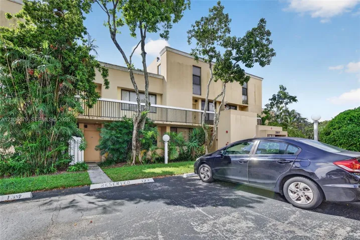 Multi-story exterior featuring a stucco facade, balcony with metal railing, and dedicated parking spaces