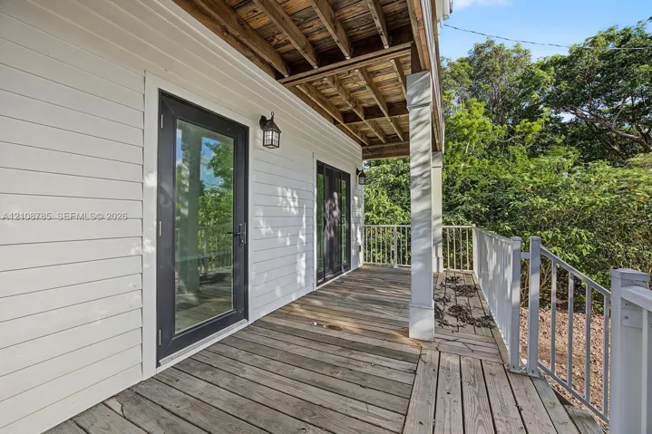 Covered wooden deck featuring horizontal siding, glass-panel exterior doors, painted square columns, and metal railings